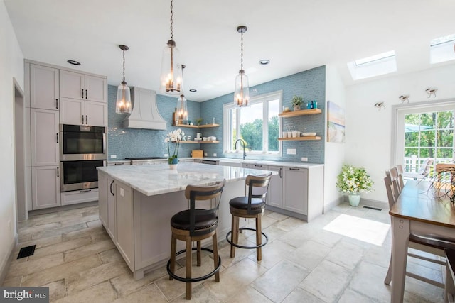 kitchen featuring backsplash, plenty of natural light, custom range hood, stainless steel double oven, and open shelves