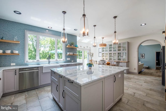 kitchen with open shelves, a sink, a kitchen island, arched walkways, and dishwasher