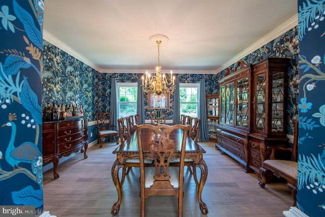 dining room featuring wood finished floors, an inviting chandelier, ornamental molding, and wallpapered walls