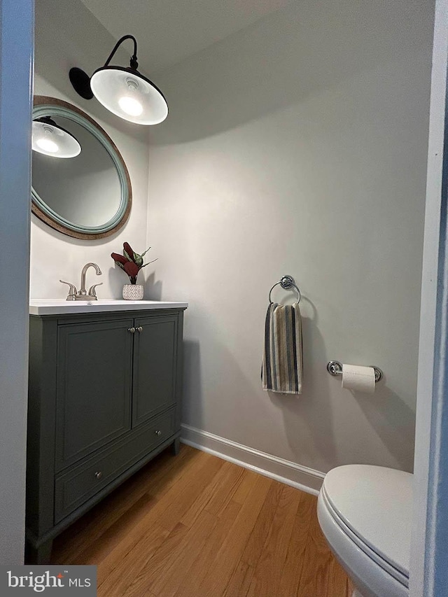 bathroom with baseboards, toilet, wood finished floors, and vanity