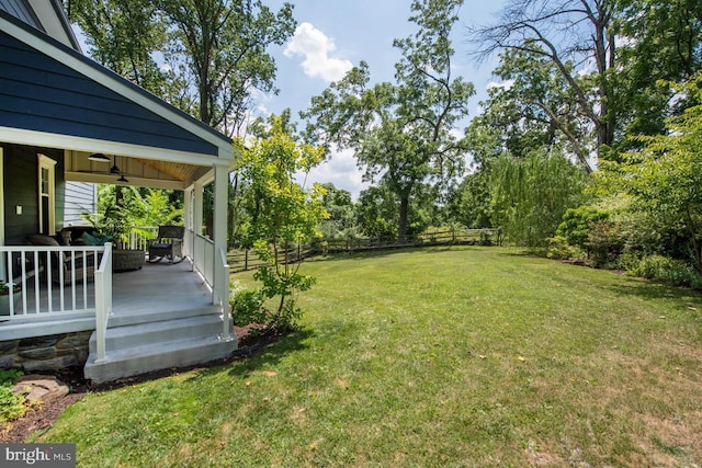 view of yard with covered porch, a ceiling fan, and fence