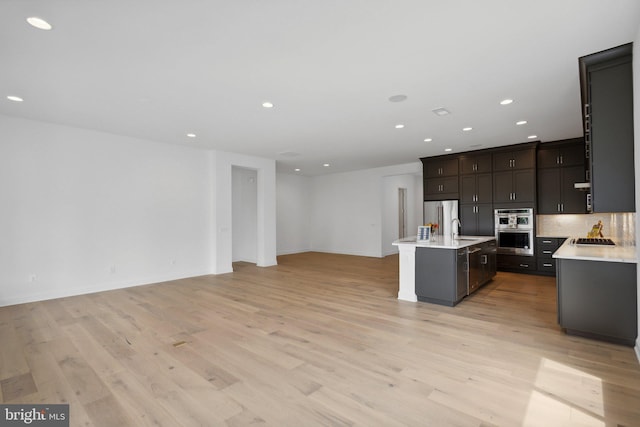 kitchen with light hardwood / wood-style floors, decorative backsplash, sink, appliances with stainless steel finishes, and an island with sink