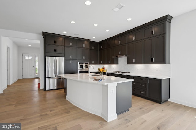 kitchen with light hardwood / wood-style floors, stainless steel appliances, a kitchen island with sink, dark brown cabinets, and sink