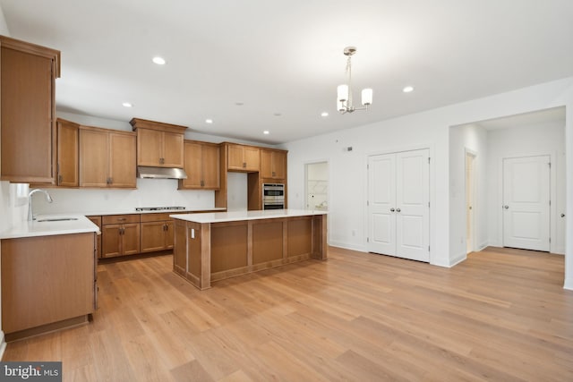 kitchen featuring decorative light fixtures, a center island, light hardwood / wood-style floors, and sink