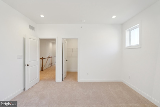 unfurnished bedroom with a walk in closet, a closet, and light colored carpet