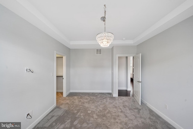 carpeted empty room featuring a chandelier and a tray ceiling