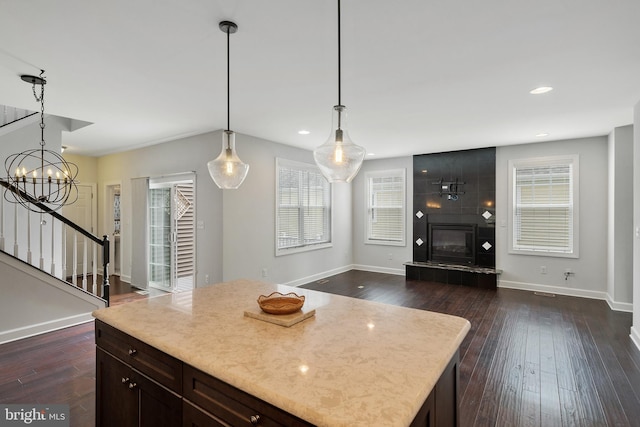 kitchen featuring dark wood-type flooring, an inviting chandelier, hanging light fixtures, a kitchen island, and a tiled fireplace