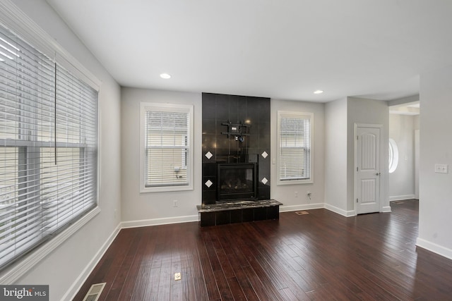 unfurnished living room featuring a tile fireplace and dark wood-type flooring