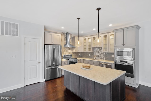 kitchen with dark wood-type flooring, wall chimney range hood, appliances with stainless steel finishes, decorative light fixtures, and a kitchen island