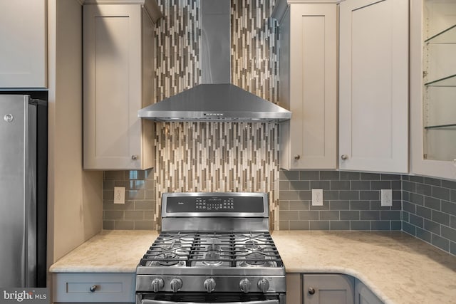 kitchen featuring light stone countertops, backsplash, stainless steel appliances, and wall chimney exhaust hood