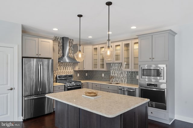 kitchen with wall chimney range hood, sink, appliances with stainless steel finishes, decorative light fixtures, and a kitchen island