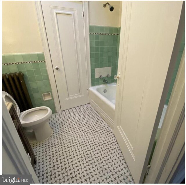 bathroom with tile patterned floors, tiled shower / bath combo, toilet, tile walls, and radiator heating unit