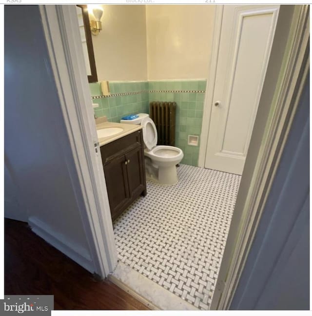 bathroom featuring radiator heating unit, tile patterned flooring, toilet, vanity, and tile walls