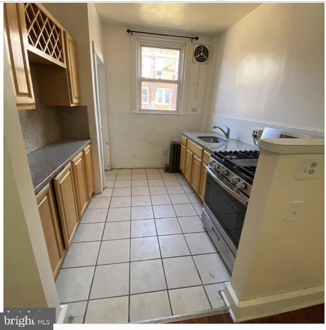 kitchen featuring light tile patterned floors, stainless steel gas range oven, and sink