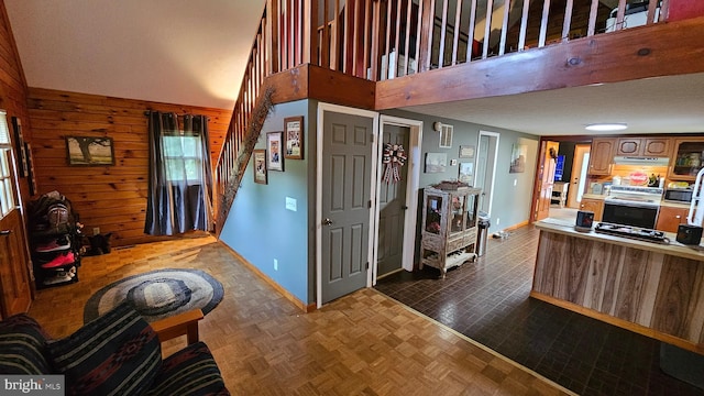 interior space with dark parquet flooring, wood walls, and a towering ceiling