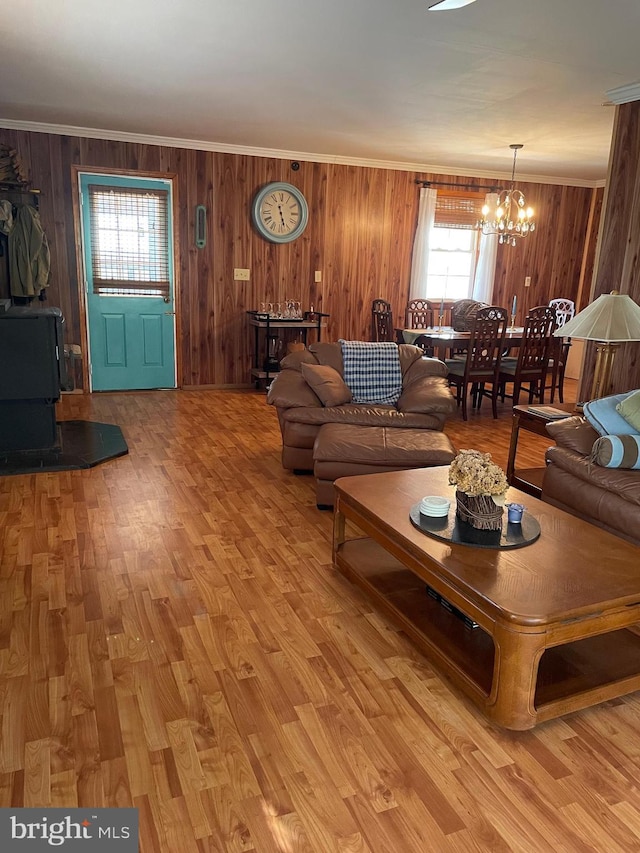 living room featuring light hardwood / wood-style floors, a wood stove, a notable chandelier, and wooden walls