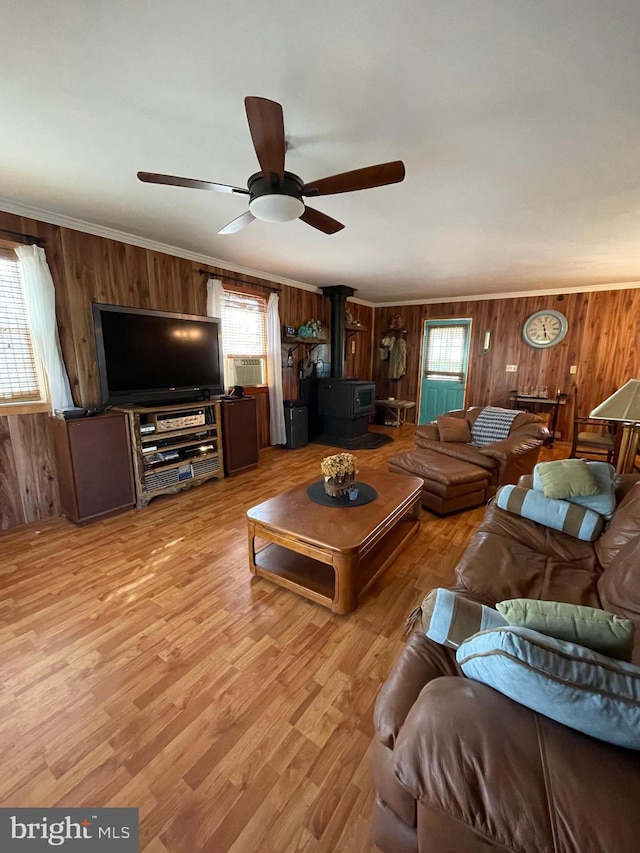 living room featuring wood walls, ceiling fan, a wood stove, ornamental molding, and light hardwood / wood-style flooring