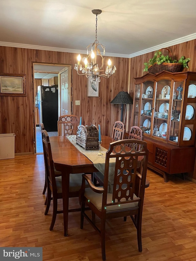 dining space featuring wood walls, crown molding, wood-type flooring, and a notable chandelier