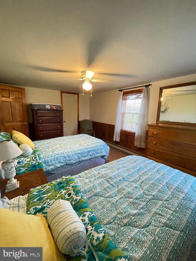 bedroom with ceiling fan, baseboard heating, and wood walls