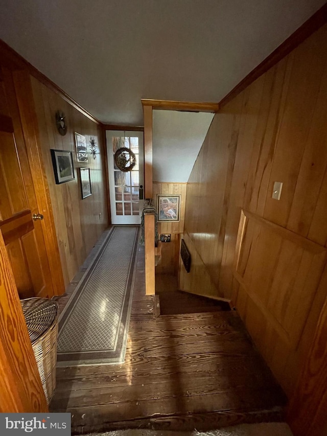 hallway with dark wood-type flooring, ornamental molding, and wood walls