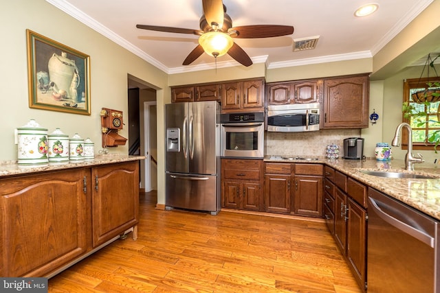 kitchen with light stone countertops, sink, stainless steel appliances, light hardwood / wood-style flooring, and ornamental molding