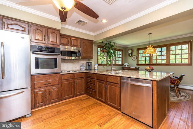 kitchen featuring kitchen peninsula, appliances with stainless steel finishes, light stone counters, and crown molding