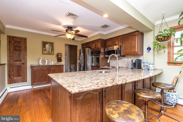 kitchen with kitchen peninsula, appliances with stainless steel finishes, ceiling fan, crown molding, and dark hardwood / wood-style floors