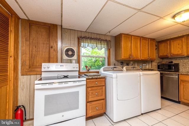 clothes washing area featuring wooden walls, light tile patterned flooring, and independent washer and dryer