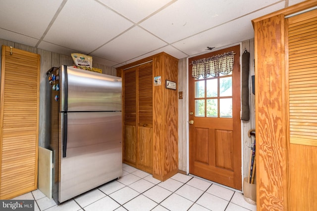 kitchen with a paneled ceiling, stainless steel fridge, wooden walls, and light tile patterned floors