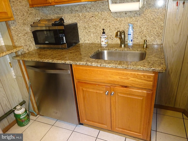 kitchen with appliances with stainless steel finishes, light tile patterned floors, light stone counters, and sink