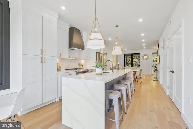 kitchen featuring wall chimney range hood, a large island, hanging light fixtures, white cabinetry, and light hardwood / wood-style floors