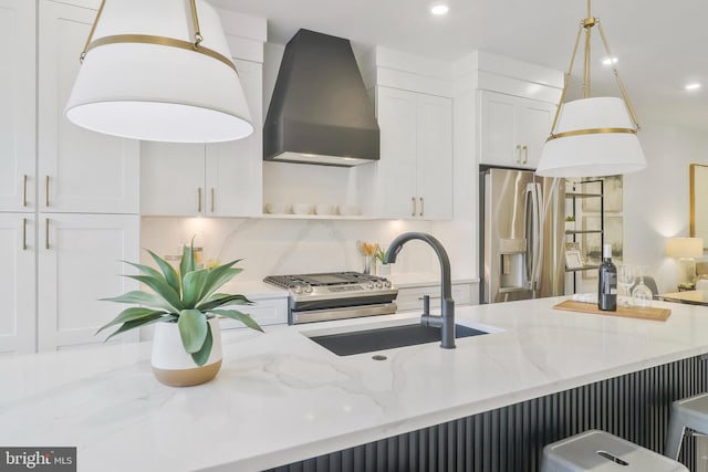 kitchen featuring wall chimney exhaust hood, hanging light fixtures, stainless steel appliances, sink, and light stone countertops