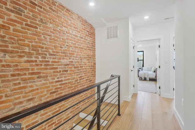 hall with brick wall and light hardwood / wood-style flooring