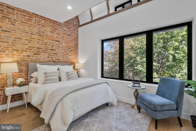 bedroom with brick wall and light hardwood / wood-style flooring