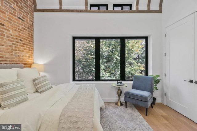 bedroom featuring light hardwood / wood-style floors, multiple windows, and brick wall