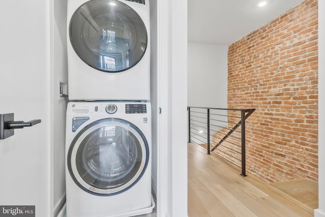 washroom featuring light hardwood / wood-style flooring, stacked washer and clothes dryer, and brick wall