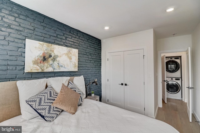 bedroom with brick wall, hardwood / wood-style floors, and stacked washing maching and dryer