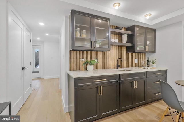 bar featuring decorative backsplash, light stone countertops, sink, and light wood-type flooring