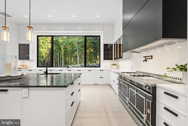 kitchen with sink, dark stone countertops, custom range hood, decorative light fixtures, and white cabinetry