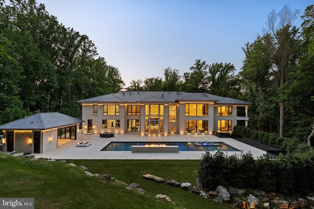 back house at dusk featuring a lawn, an outdoor living space with a fire pit, a patio, and a pool with hot tub