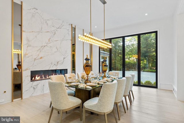 dining space with a fireplace, light wood-type flooring, and a wall of windows