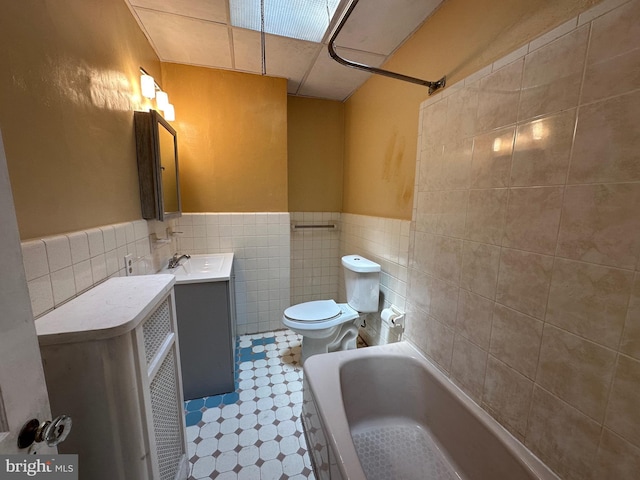 bathroom with vanity, a tub to relax in, toilet, and tile walls