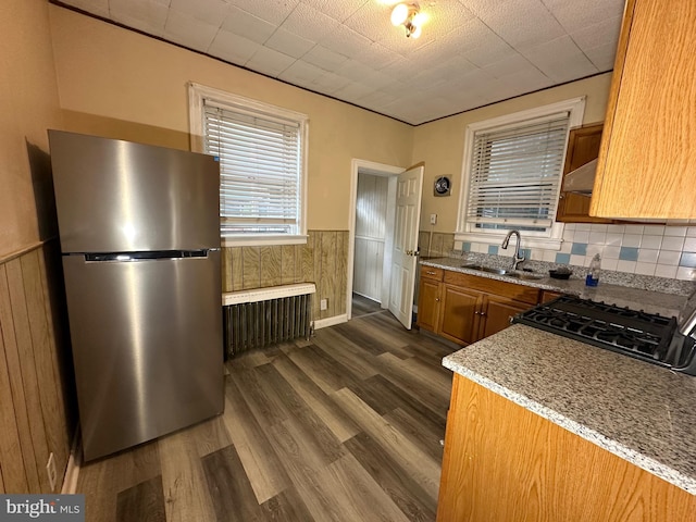 kitchen with stove, radiator, sink, light stone counters, and stainless steel refrigerator