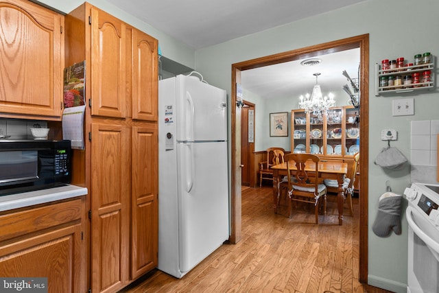 kitchen featuring white appliances, decorative light fixtures, light hardwood / wood-style flooring, and a notable chandelier