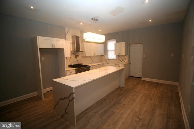 kitchen with white cabinets, wall chimney range hood, light stone countertops, decorative light fixtures, and a kitchen island