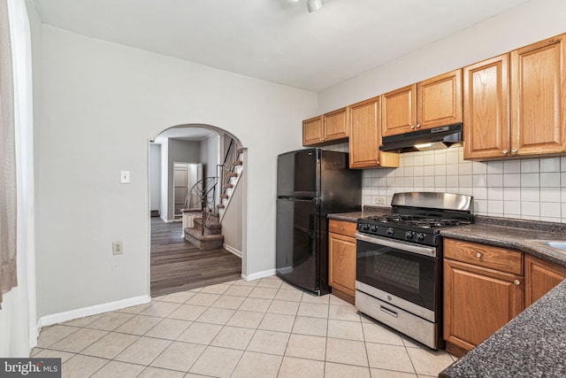 kitchen featuring black refrigerator, light tile patterned floors, backsplash, and stainless steel range with gas stovetop