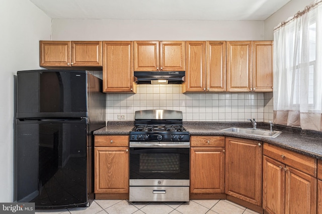 kitchen with decorative backsplash, black fridge, sink, light tile patterned floors, and stainless steel range with gas cooktop