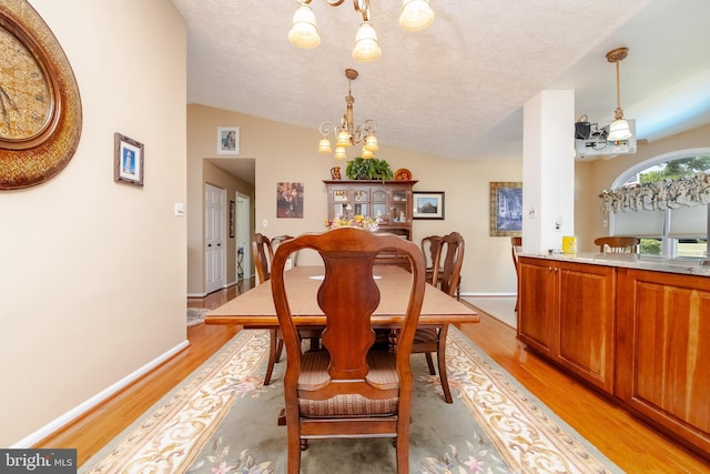 dining area with vaulted ceiling, light hardwood / wood-style flooring, and an inviting chandelier