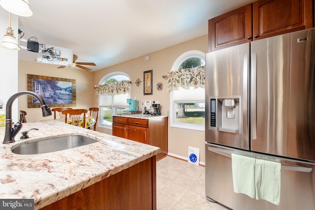 kitchen with sink, stainless steel refrigerator with ice dispenser, hanging light fixtures, ceiling fan, and light stone countertops