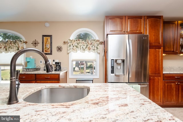 kitchen featuring stainless steel fridge, light stone countertops, and sink